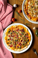 Fresh homemade pizza with prosciutto, capers, olives on a wooden background in composition with a red cloth and olive oil. Italian Cuisine. Top view food photo