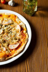 Fresh homemade pizza with ham, mushrooms and olive on a wooden background in composition with a red cloth and olive oil. Italian Cuisine. Selective focus on center of pizza