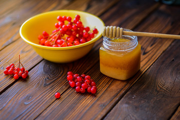 A jar of honey with a honey dipper and red arrow-wood berries