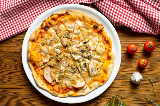 Fresh homemade pizza with ham, mushrooms and olive on a wooden background in composition with a red cloth and olive oil. Italian Cuisine. Top view food photo