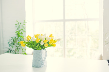 A bouquet of tulips in a pot in the form of a teapot on a white table. Taken in warm daylight.