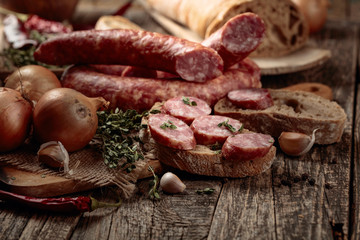 Dry-cured sausage with bread and spices on a old wooden table.