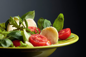 Green salad with mozzarella, tomato, basil and olive oil in green plate.