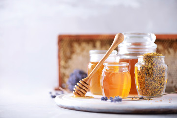 Bee pollen granules, honey jar with wooden dropper, honeycomb on grey backdrop. Copy space. Autumn harvest concept