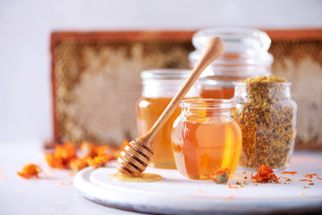 Herbal honey in jar with dipper, honeycomb, bee pollen granules, calendula flowers on grey...