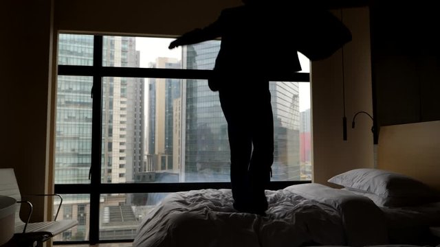 Man jump on bed like crazy, celebrate some achievement. He caper around, then pull off suit and send it fly, fall down on bed. Slow motion shot