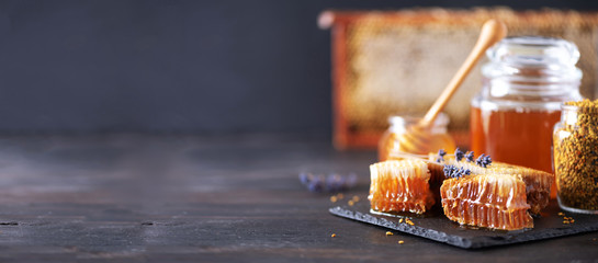 Honeycomb and honey jar with dipper on black slate tray over dark backdrop. Copy space. Top view.
