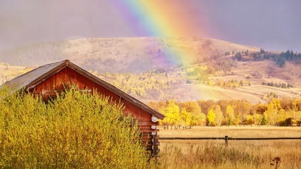 A beautiful autumn landscape scene in rural Wyoming, as a rainbow fills the sky behind an old...