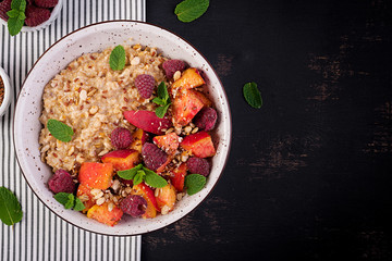 Oatmeal porridge with raspberry and peach on dark background. Healthy breakfast. Vegetarian food....