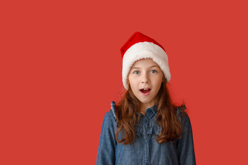 Surprised little girl in Santa Claus hat on color background