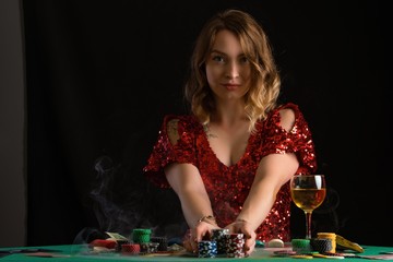 Girl in evening red dress plays poker. Gaming business in a casino or night club. On a black background for design, with smoke.
