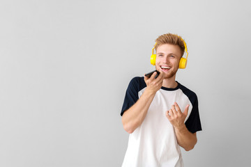 Handsome young man listening to music on light background