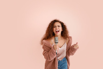 Beautiful African-American female singer with microphone on color background