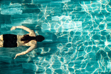 Top view of a long haired man swimming laps on a pool