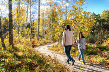 Mother and little girl walking together on the wooden walkway on a sunny autumn day.