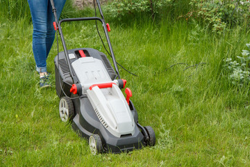 Woman is operating with lawn mower in the garden