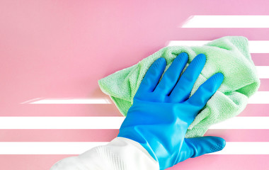 A hand in a blue protective rubber glove rubs the pink surface with white stripes with a green microfiber cloth and scrubs the white stripes. concept of purity and freshness, new surface