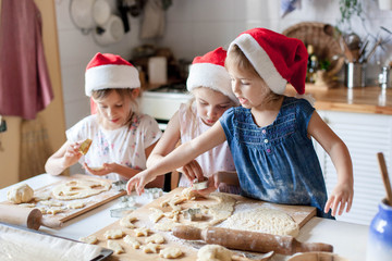 Kids cooking Christmas gingerbread cookies in cozy home kitchen. Funny children chefs in santa hats prepare holiday food. Cute girls make homemade cake. Lifestyle authentic moment. Family traditions.