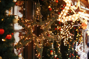 Stylish christmas star illuminated and fir branches with red and gold baubles, golden lights bokeh...