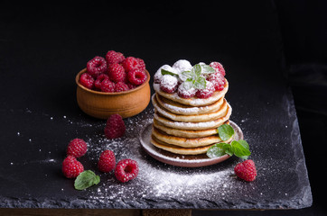 Pancakes with raspberries and berries around on black backgound