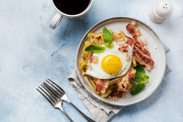 Cheese Waffles with fried bacon, egg and parmesan cheese with spices and basil for breakfast on light old concrete background. Top view.