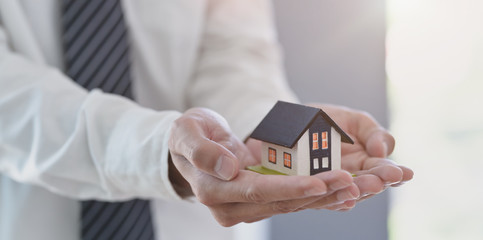Property insurance concept : insurance agent holding a house model in his hand
