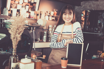 Young asian women barista holding blank chalkboard menu and smiling at coffee shop counter background, start up small business owner food and drink concept
