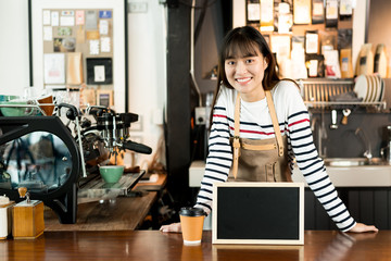 Young asian women barista holding blank chalkboard menu and smiling at coffee shop counter...