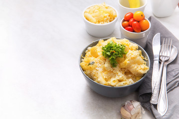 Baked mac and cheese inside a bowl, served on the dining table, next to cherry tomatoes and olive oil, with negative space next to it.
