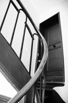 Typical narrow spiral staircase with railing in old Parisian house and flat door. Selective focus. Black and white photo.