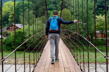 Man travels backpacking, walking on a suspension bridge in mountains village