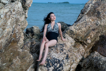 Pretty Asian woman in swimming suit posing on the stone of beach with fun.