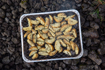 Potatoes are cooked on disposable grill. Small foil barbecue stands on the stones. Preparing BBQ, Iceland