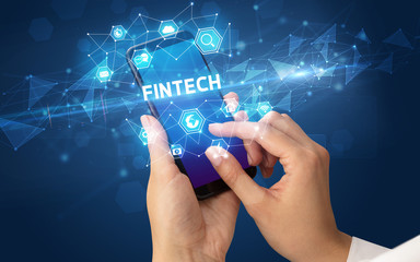 Female hand holding smartphone with FINTECH inscription, modern technology concept
