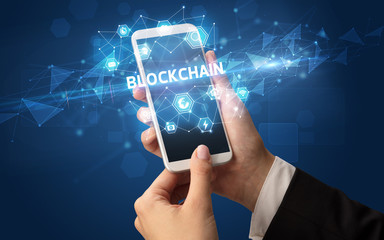 Female hand holding smartphone with BLOCKCHAIN inscription, modern technology concept