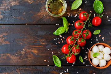 Fresh cherry tomatoes, basil leaves, mozzarella cheese and olive oil on old wooden background. Caprese salad ingredients. Selective focus.