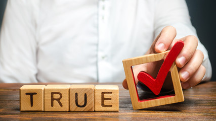 A man holds a red check mark over word True. Confirm the veracity and truth. Fight against fake...