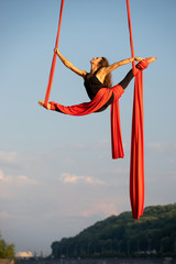 Beautiful and flexible female circus artist dancing with aerial silk on a sky background