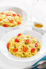 Pesto spaghetti with cherry tomatoes on top of served restaurant table.