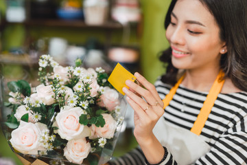Smiling woman florist, small business flower shop owner, at counter, looking friendly at camera working at a special flower arrangement.
