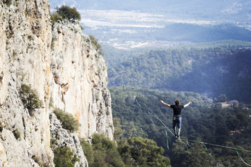 A man is walking along a stretched sling. Highline in the mountains. Man catches balance. Performance of a tightrope walker in nature. Highliner on the background of the mountains.