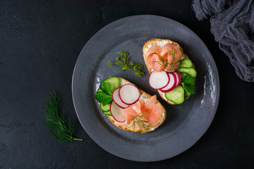 Sandwiches with smoked pink salmon, radish, cucumber and cream cheese on gray ceramic plate and textile background. Traditional Scandinavian toast. Top view.Square image
