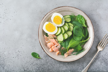 Scandinavian salad with smoked pink salmon, spinach, cucumber and chicken egg in gray ceramic dish. Top view. Toned image.