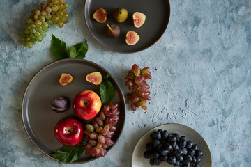 Assortment healthy organic fruits in plates apple grapes fig plums tangerines