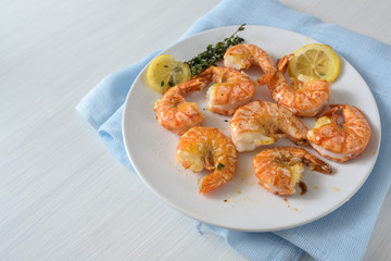 Roasted tiger prawn shrimps with garlic, lemon and herbs on a white plate, copy space