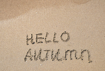 The words Hello autumn written on sand.