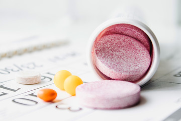 Large pink pills or vitamins near a jar on a calendar background.