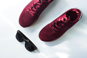Pair of burgundy sneakers shoes and black sunglasses top view, flatlay. Sport concept, casual style.