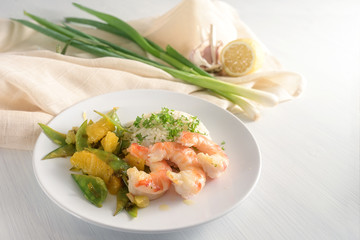 fried tiger prawn shrimp dish with sugar peas, onion and oranges served with rice on a white table, copy space