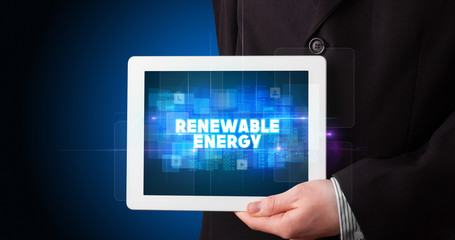 Young business person working on tablet and shows the inscription: RENEWABLE ENERGY